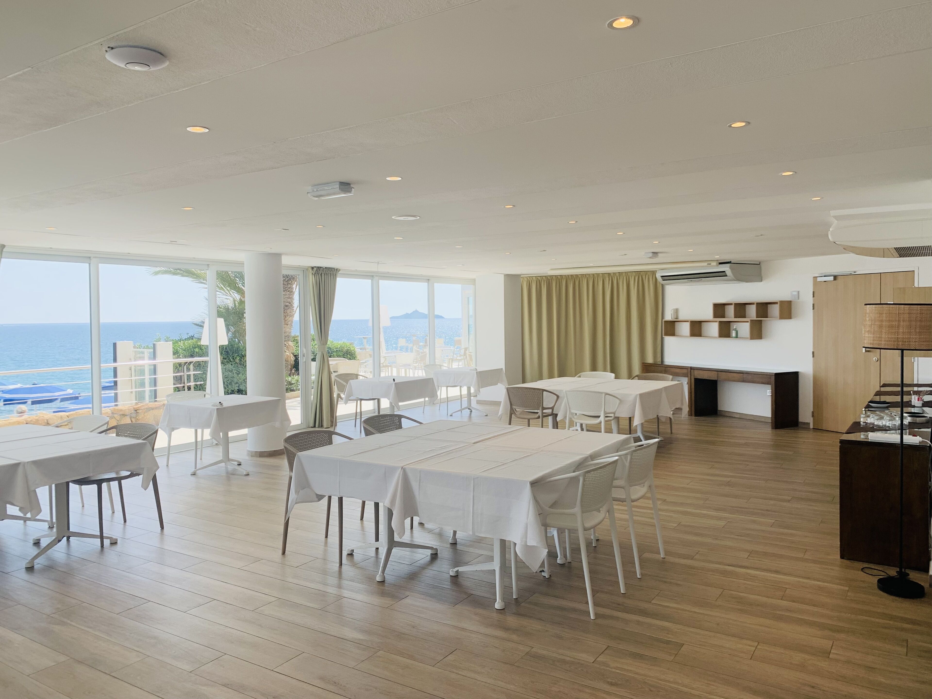 Uma ampla área de jantar com mesas e cadeiras, grandes janelas com vista para o mar e design de interiores moderno.