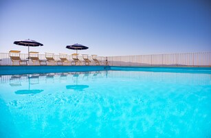 Una piscina con sillas de descanso y sombrillas, rodeada por una valla.
