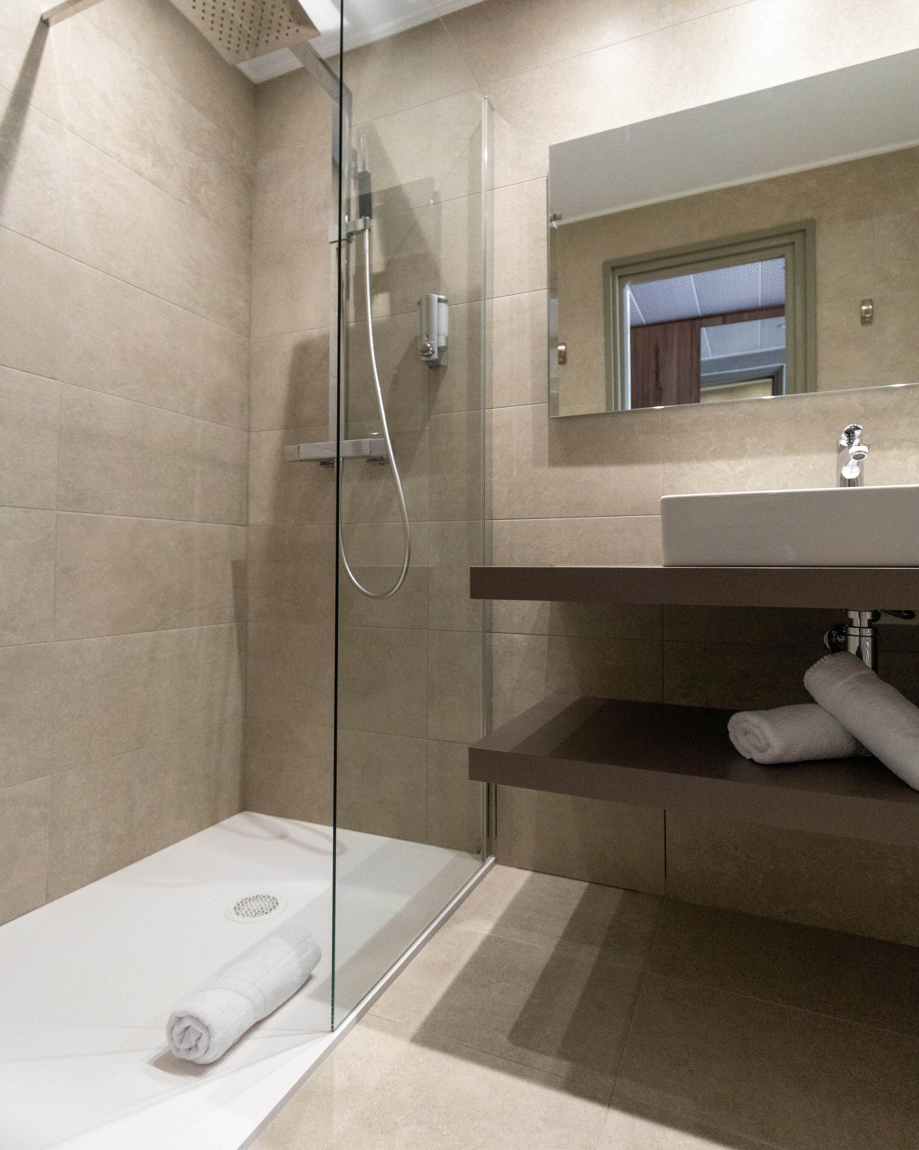A modern bathroom with a glass shower enclosure, a sink with a mirror above it, and a towel on the floor.