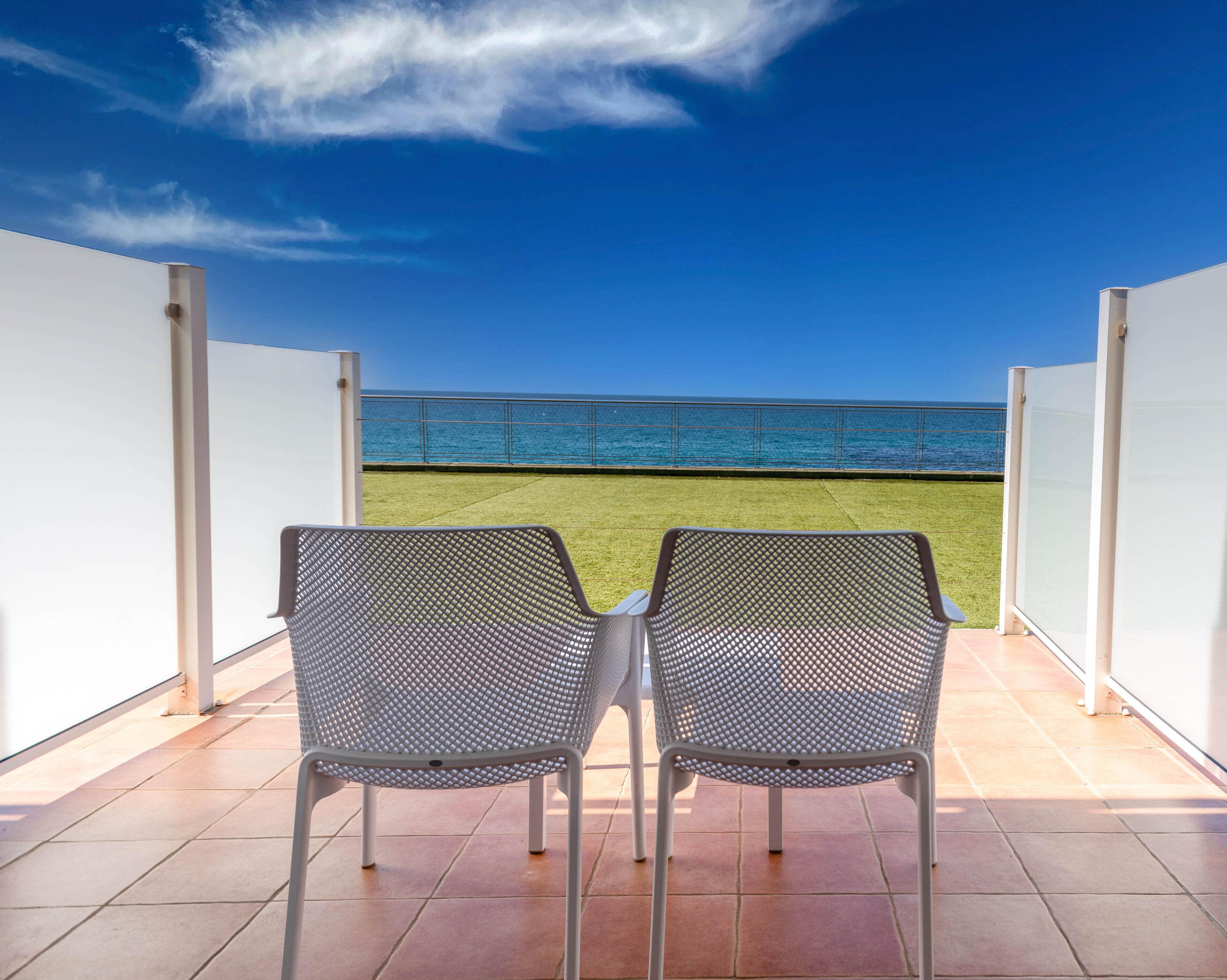 Two metal chairs facing a balcony with a view of the sea.