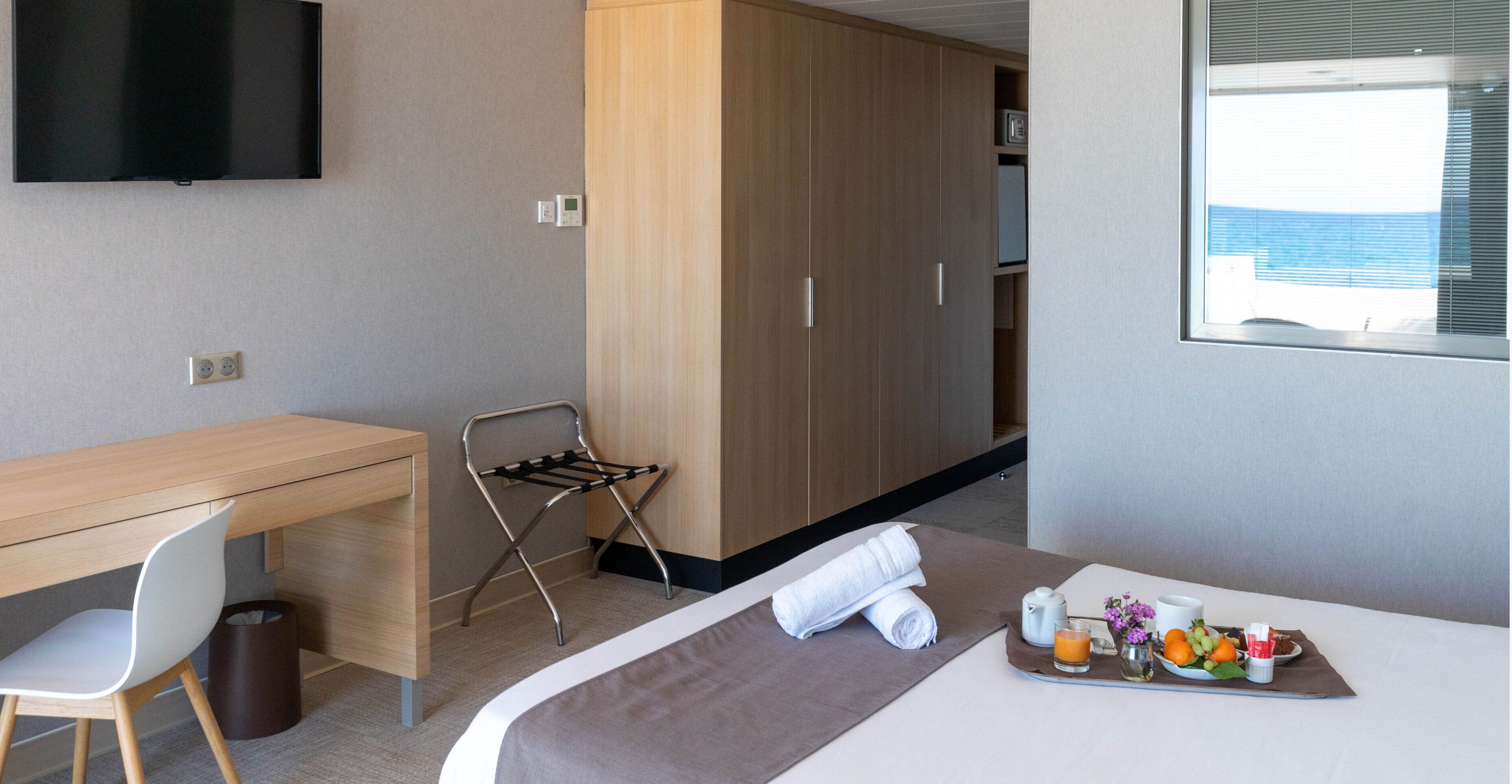 A hotel room with a bed, a desk, a TV, a wardrobe, and a breakfast tray.