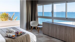 Ein Hotelzimmer mit großem Fenster und Meerblick, einem Bett mit einem Frühstücksbrett, einem kleinen Tisch und einem Sessel.
