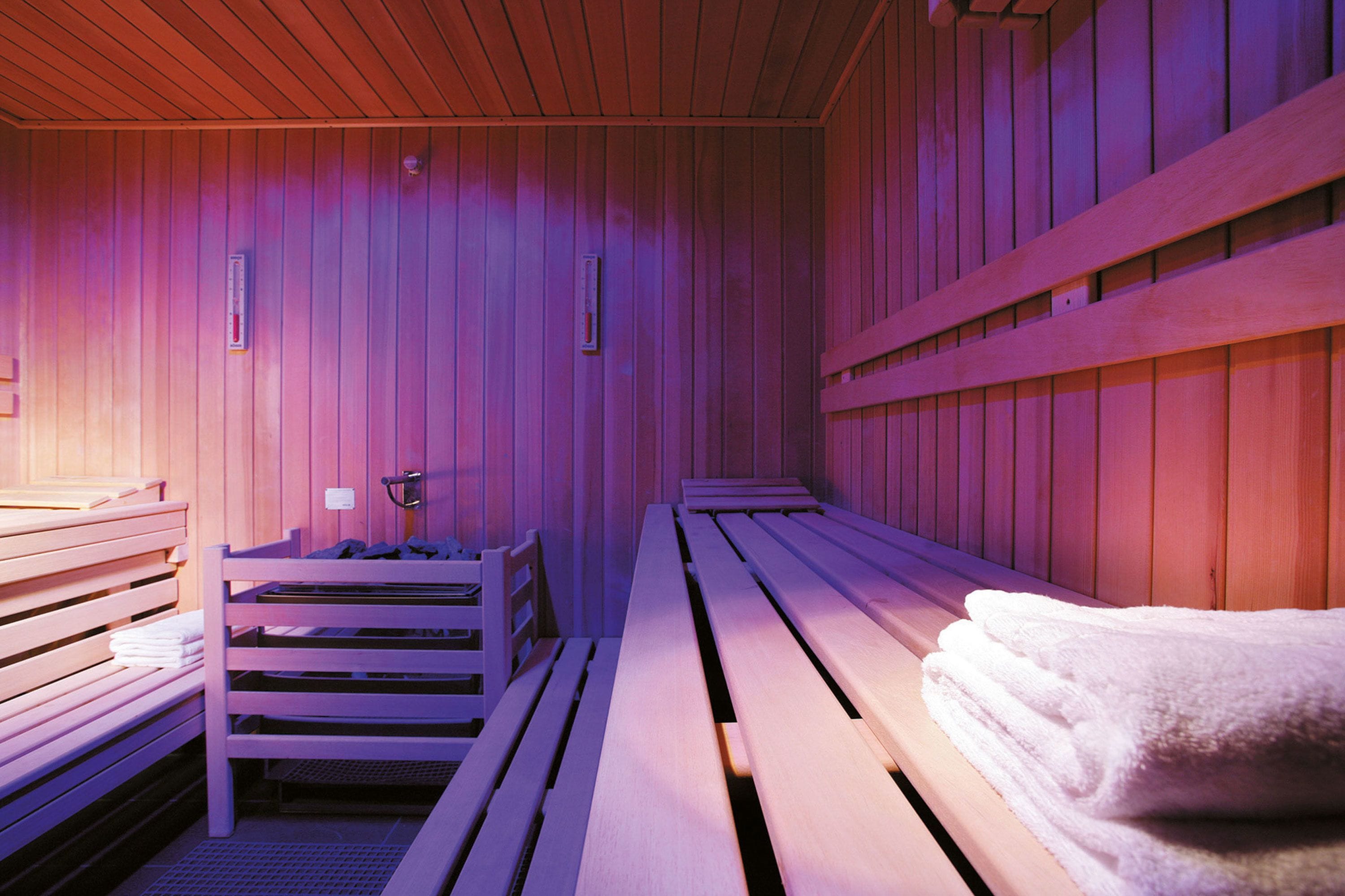 A sauna room with wooden benches, a bench with towels, and a bench with a towel rack.
