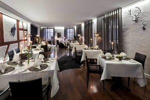 Un restaurante con varias mesas dispuestas para comer, con manteles blancos, velas y centros de mesa.