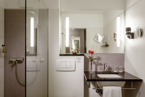 A bathroom with a glass shower enclosure, a sink with a mirror, and a towel rack.