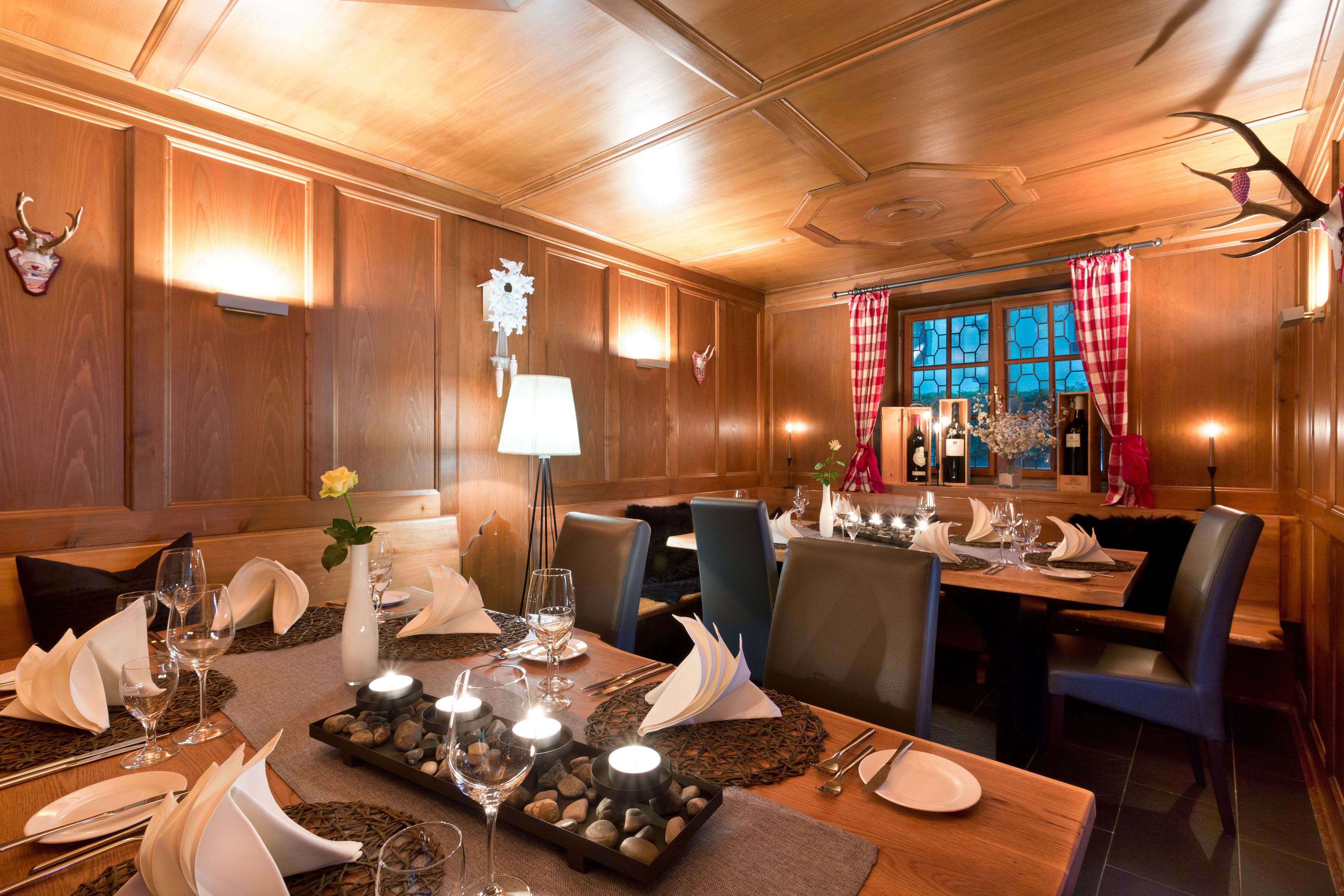 Un comedor bien iluminado con paneles de madera, una araña y vista al exterior a través de una ventana con cortina a cuadros rojos y blancos.
