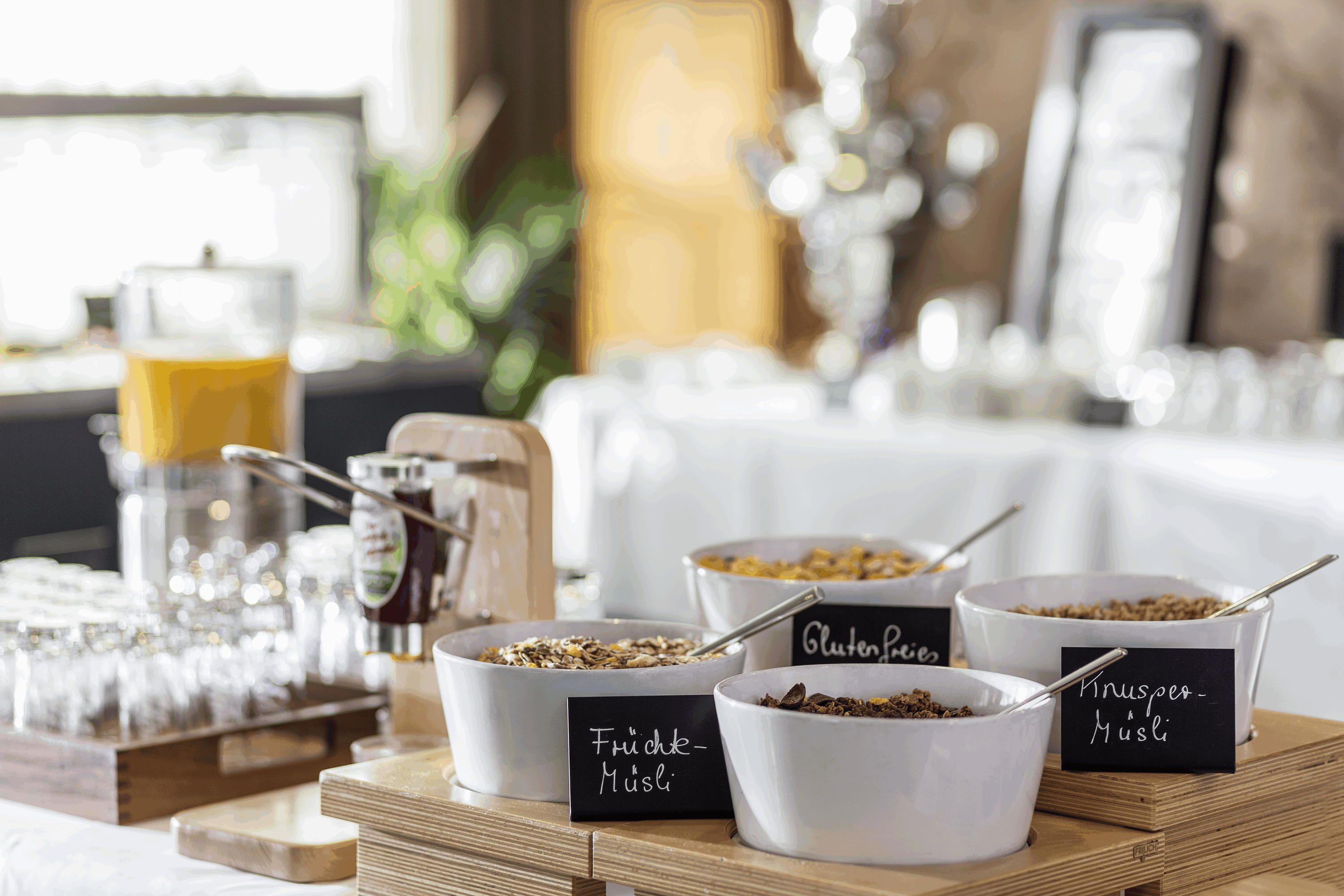 A breakfast buffet with labeled bowls of granola, including gluten-free and nut-free options.