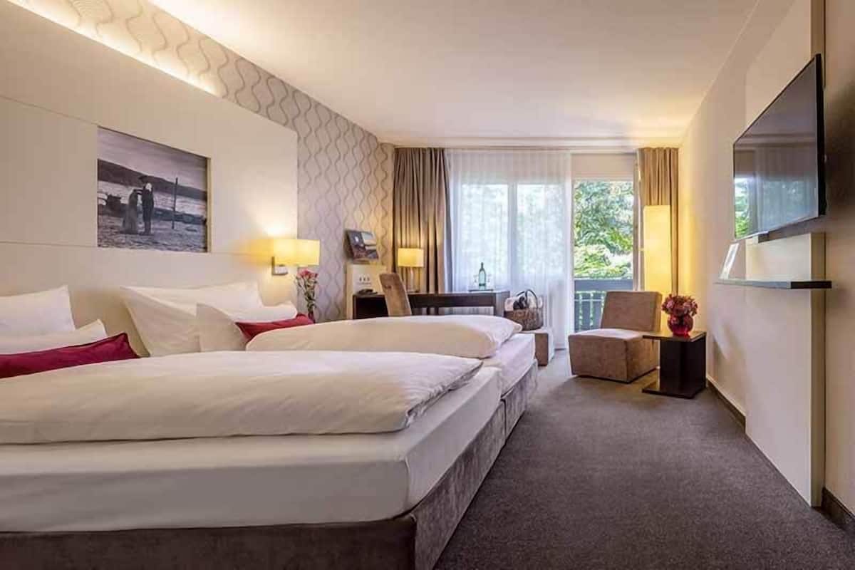 A hotel room with two beds, a desk, a chair, a TV, and a window with curtains.