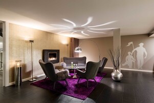 Una sala de estar moderna con chimenea, una mesa de centro redonda, dos sillones y un tapete morado.