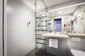 Uma casa de banho moderna com cabine de duche em vidro, um lavatório e uma toalha pendurada na parede, e uma sanita.