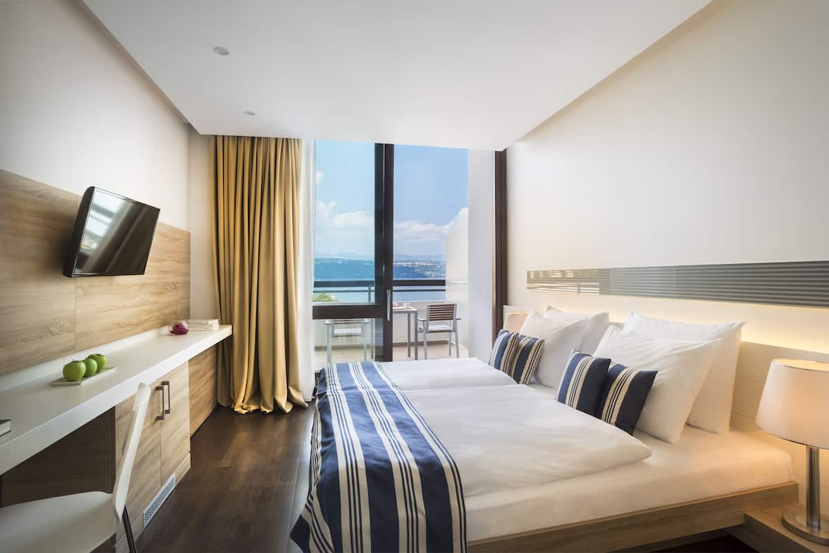 Een moderne hotelkamer met een groot bed, een aan de muur bevestigde televisie, een balkon met uitzicht en een klein bureau.