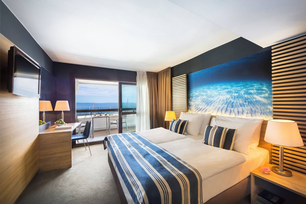 Een hotelkamer met een groot bed, een bureau, een stoel, een televisie en uitzicht op de oceaan.