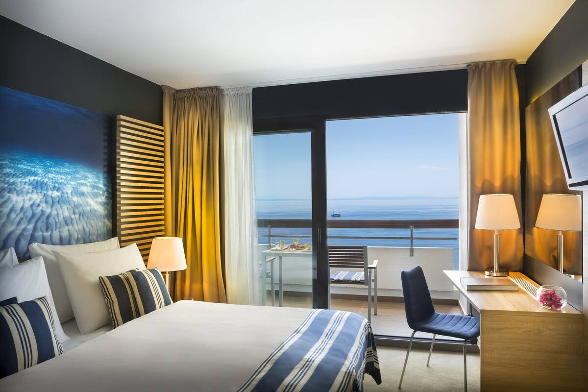 Een hotelkamer met een bed, een bureau, een stoel, een tafel met een laptop en uitzicht op de oceaan.