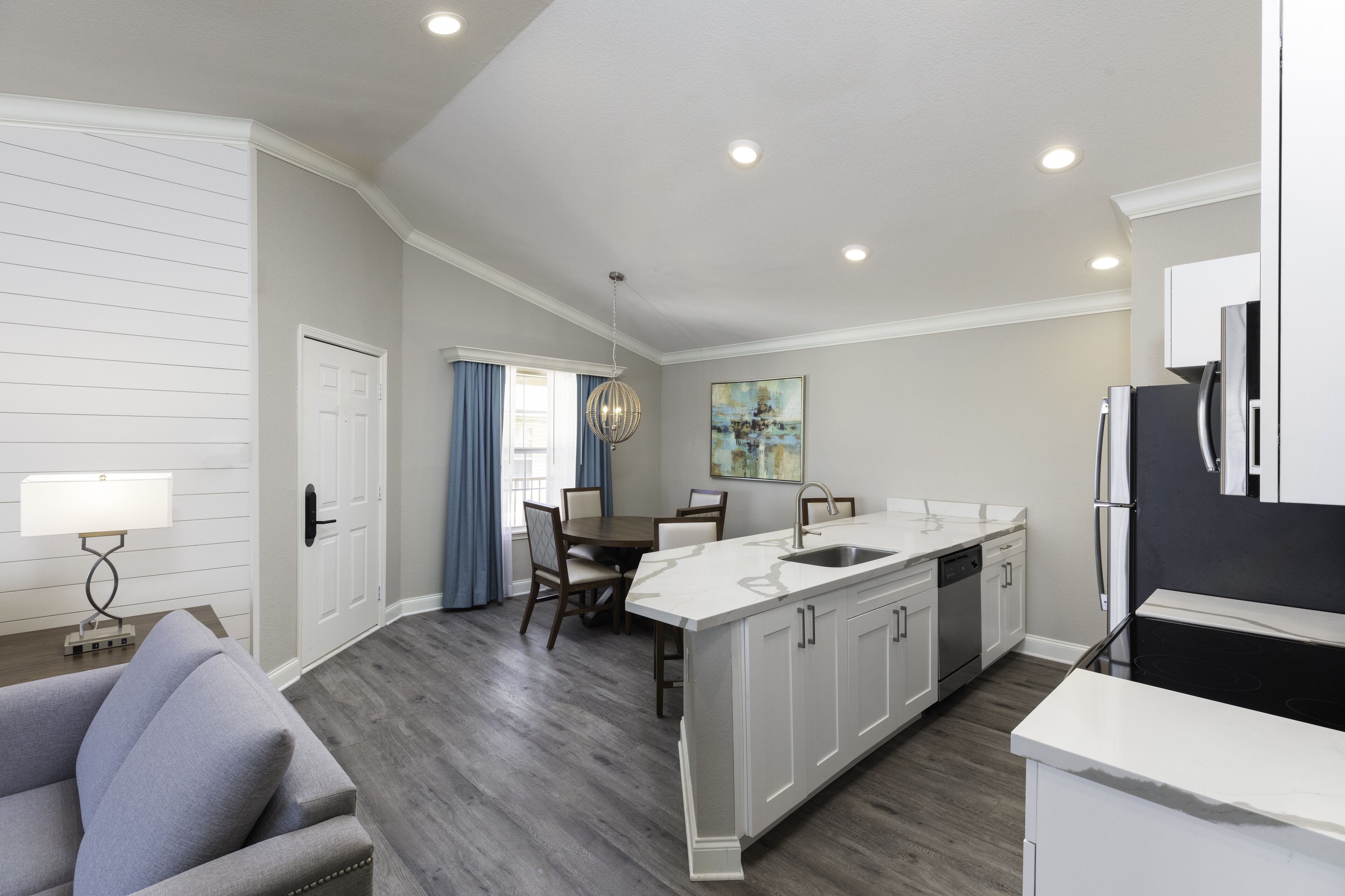 A modern kitchen with white cabinetry, a black refrigerator, and a dining area with a table and chairs.