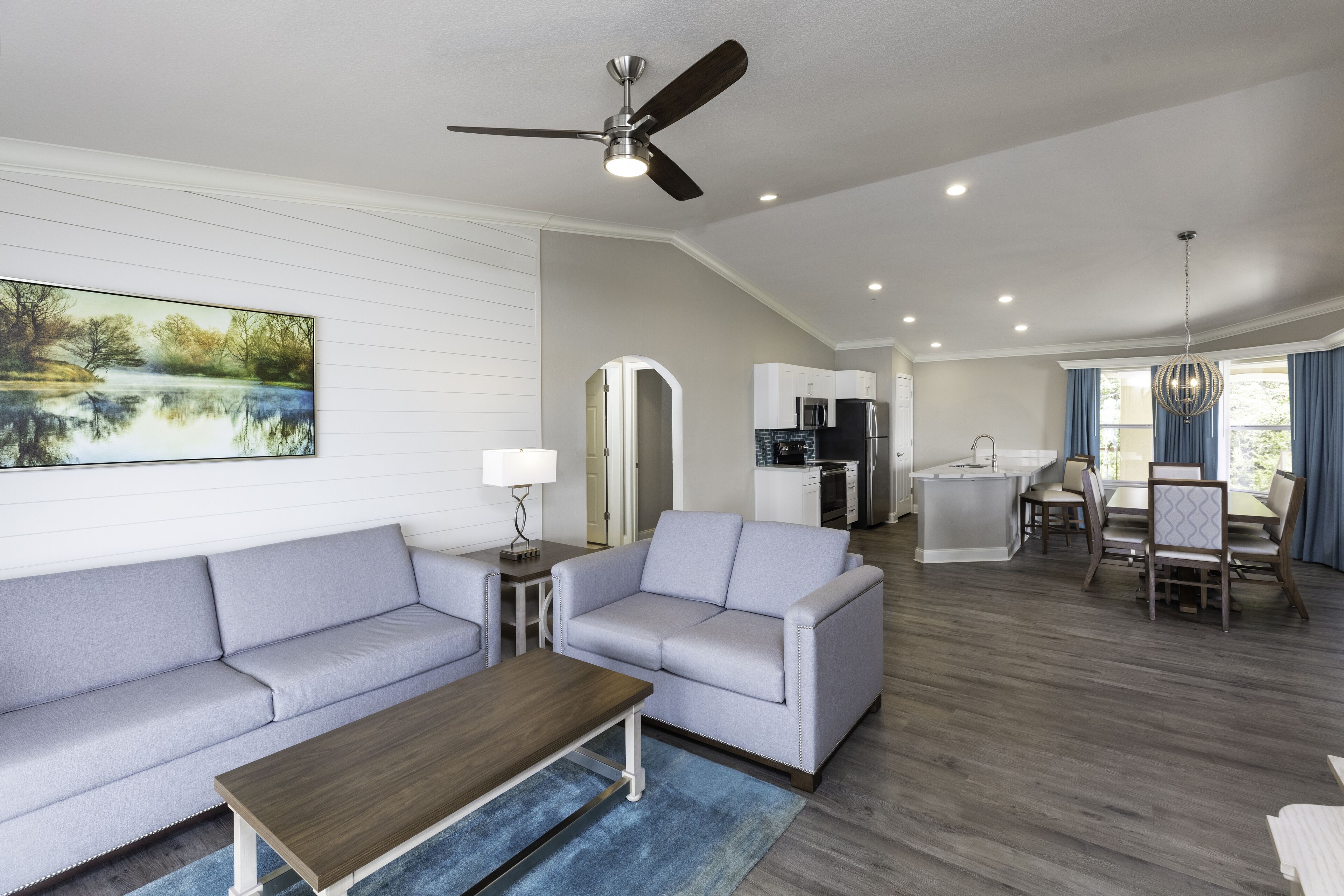 A spacious living area with a sofa, coffee table, and a dining table with chairs. There is a kitchen area with a refrigerator and a dining table.