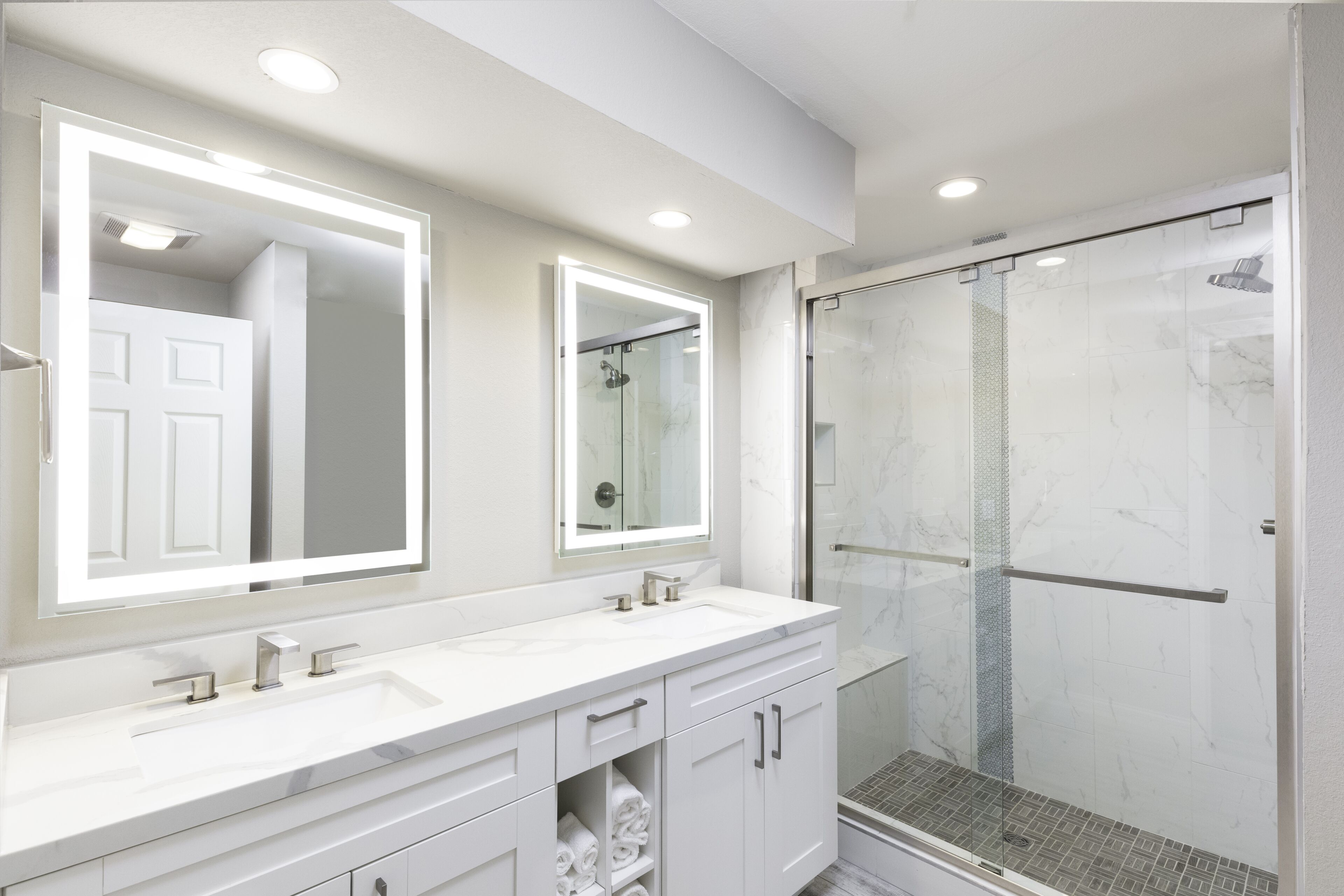 A modern bathroom with a double sink vanity, a large mirror, and a glass-enclosed shower.