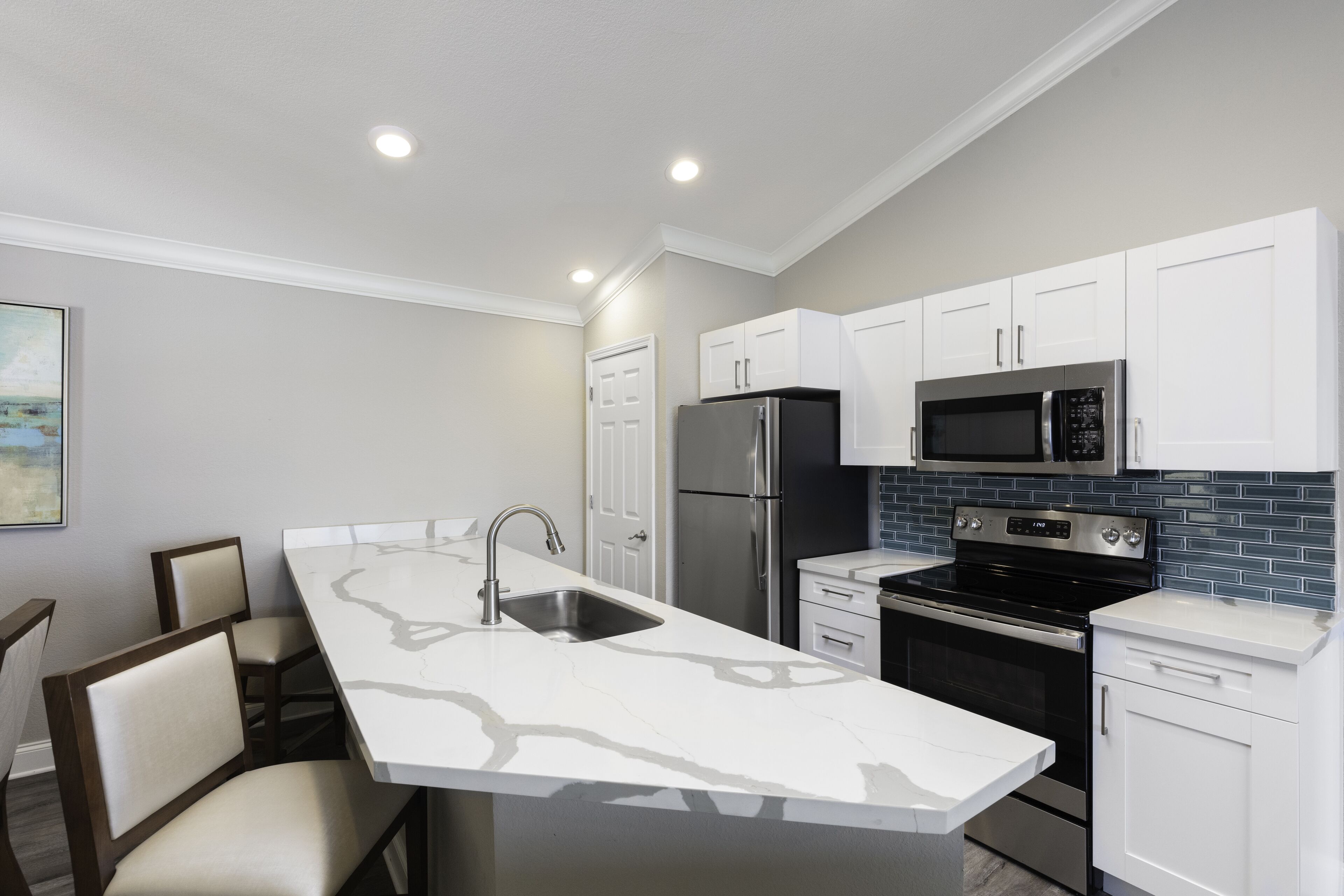 A modern kitchen with white cabinets, stainless steel appliances, and a marble countertop.