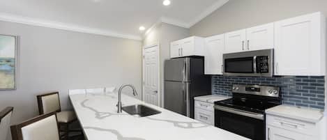 A modern kitchen with white cabinets, stainless steel appliances, and a marble countertop.