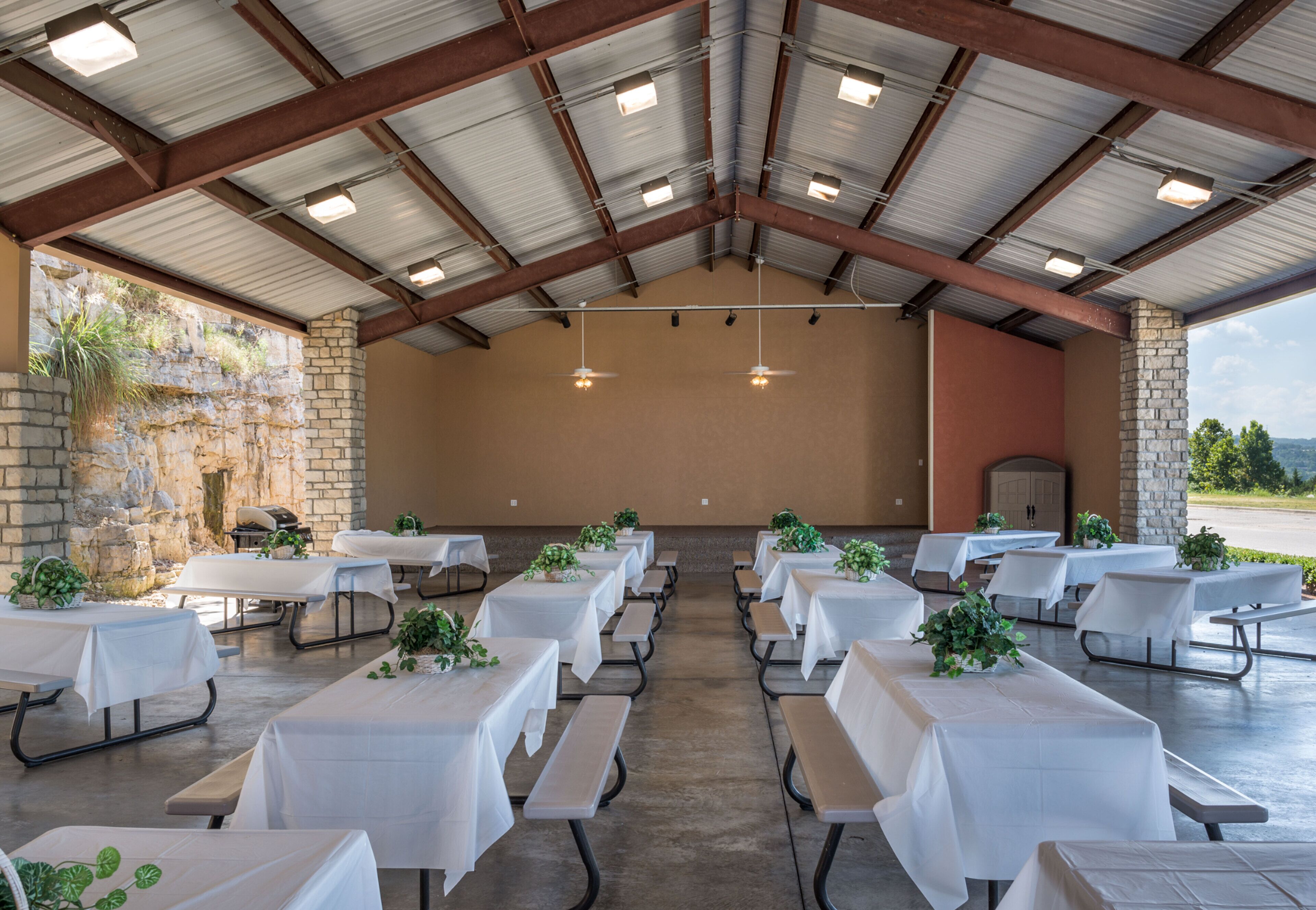 An indoor event space with tables and benches, a stone wall, and a view of the outdoors.