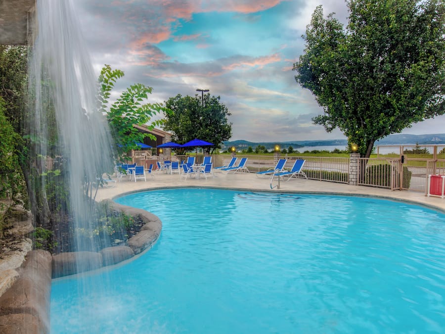 A swimming pool with a waterfall feature, surrounded by lounge chairs and a view of a distant landscape.