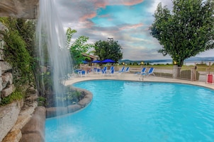 Piscina con cascada, rodeada de sillas de descanso y vistas a un paisaje distante.