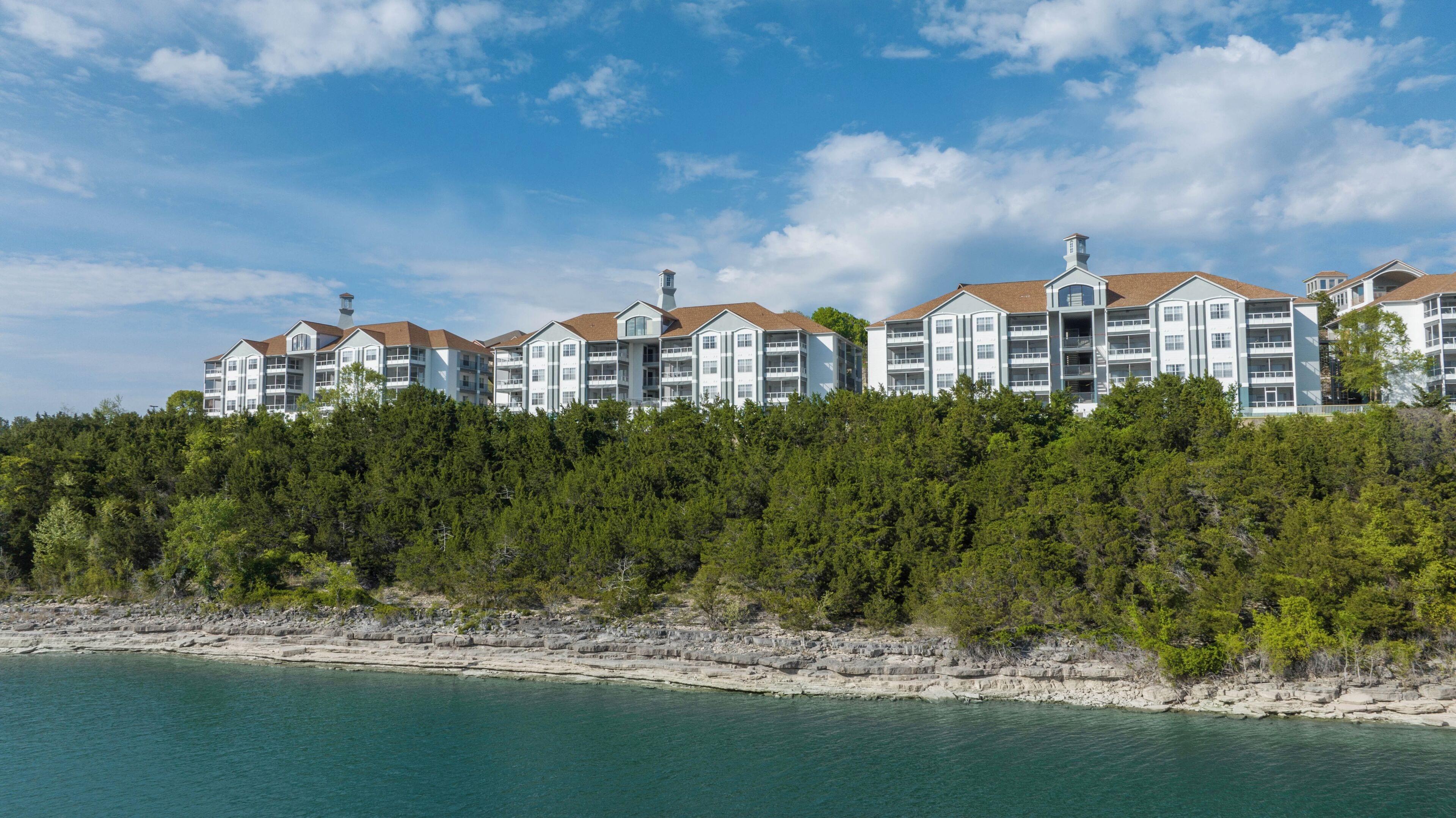 A multi-story hotel with balconies, located on a rocky shoreline with a view of the sea.