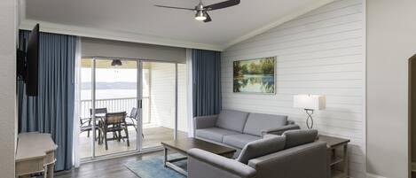 Un soggiorno moderno con un divano grigio, un tavolino da caffè e una ventola a soffitto. Si intravede un balcone con tavolo e sedie attraverso le porte in vetro.