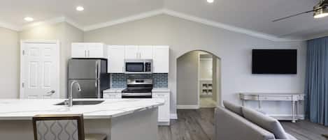 Una cocina moderna con armarios blancos, microondas integrado y un refrigerador de acero inoxidable.