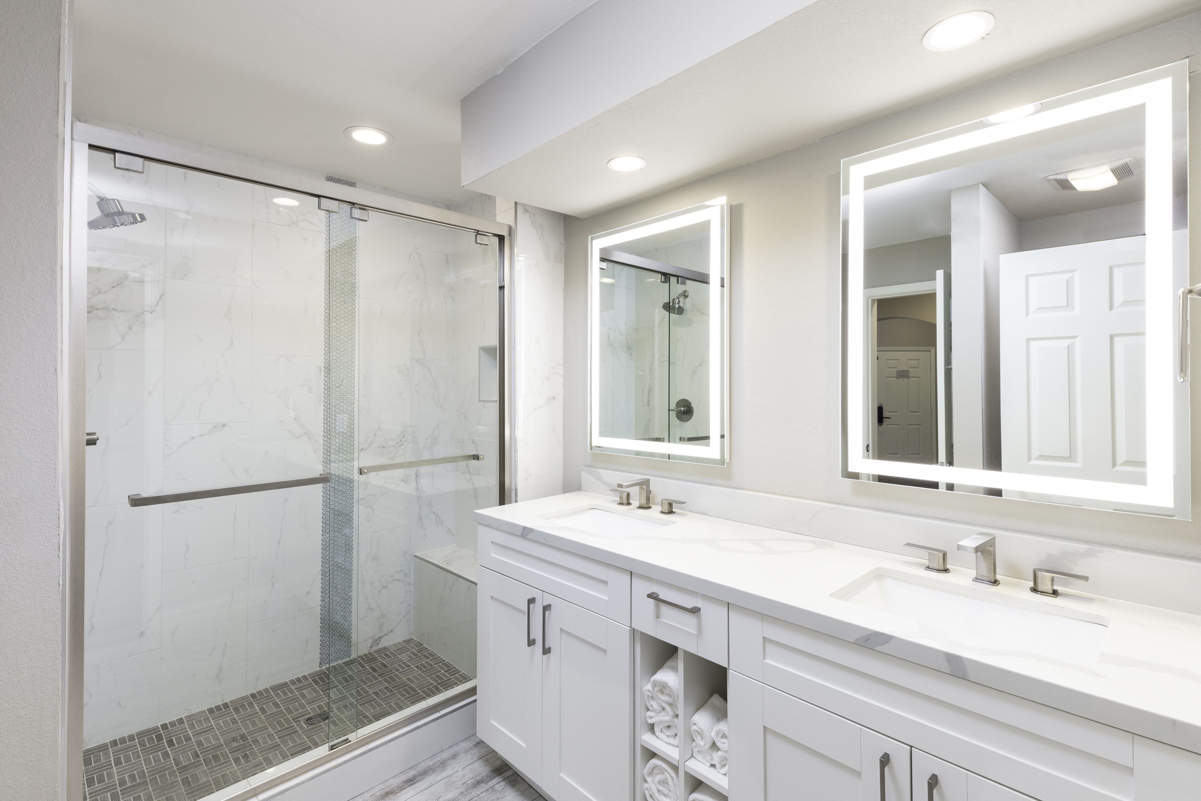 A modern bathroom with a glass-enclosed shower, a double sink vanity, and a large mirror above the vanity.