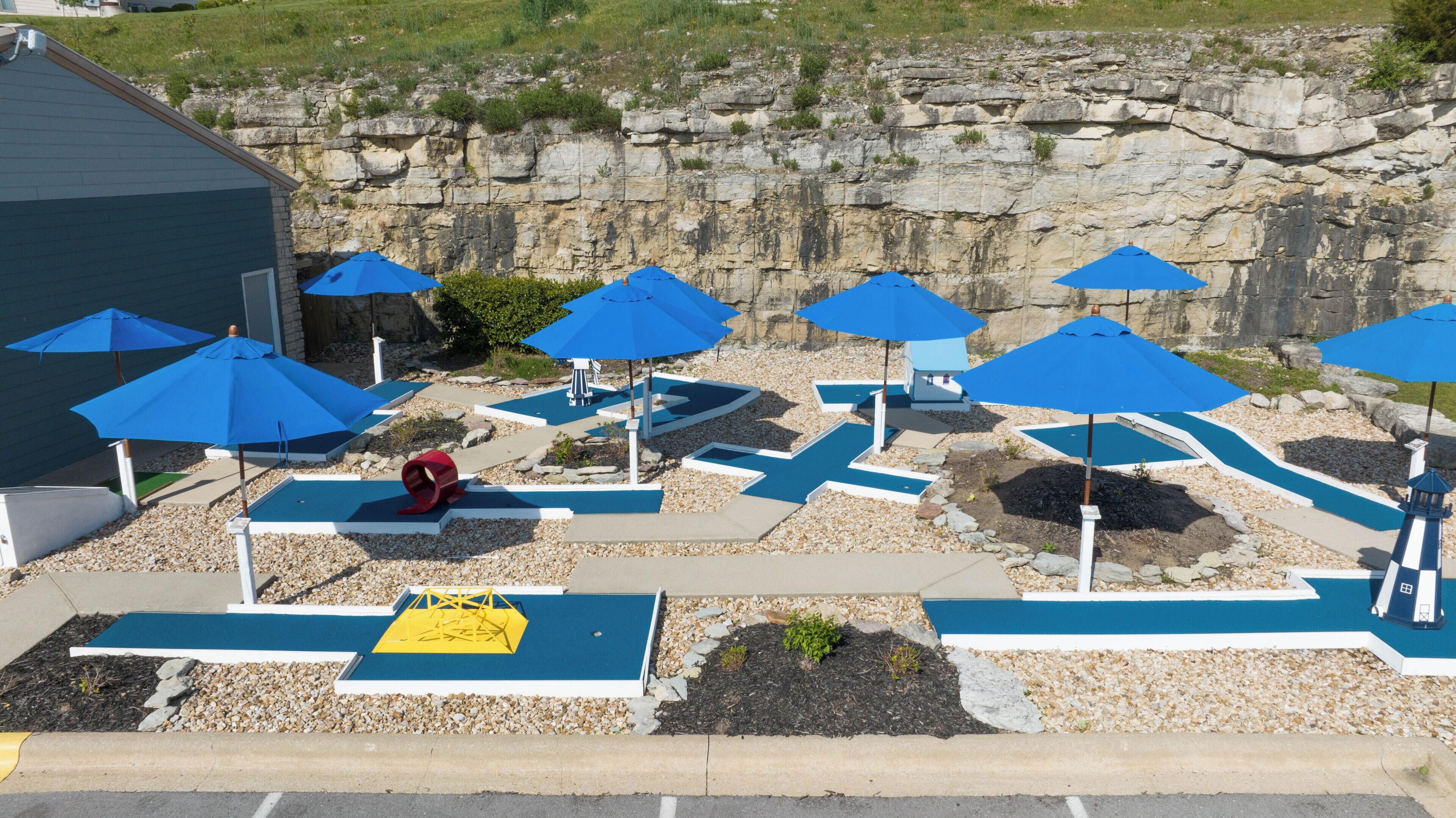 Zona de piscina con múltiples sombrillas azules, una escultura roja y un telón de fondo rocoso.