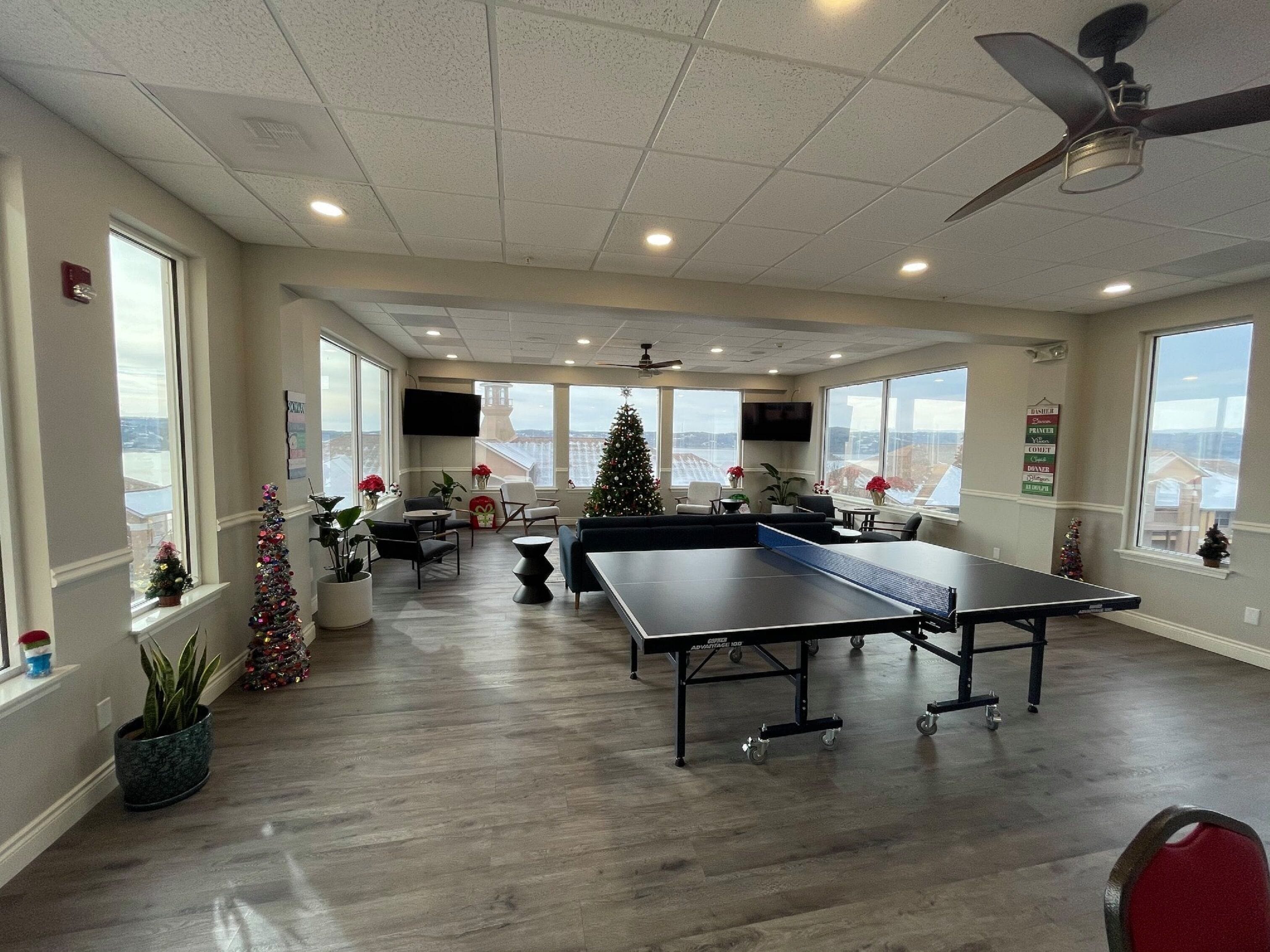 A spacious room with a ping pong table, seating area, and large windows offering views.