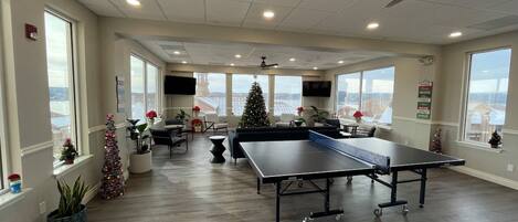 A spacious room with a ping pong table, seating area, and large windows offering views.