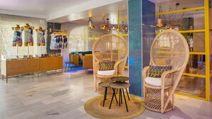A modern hotel lobby with wicker chairs, a wooden reception desk, and a patterned wall.