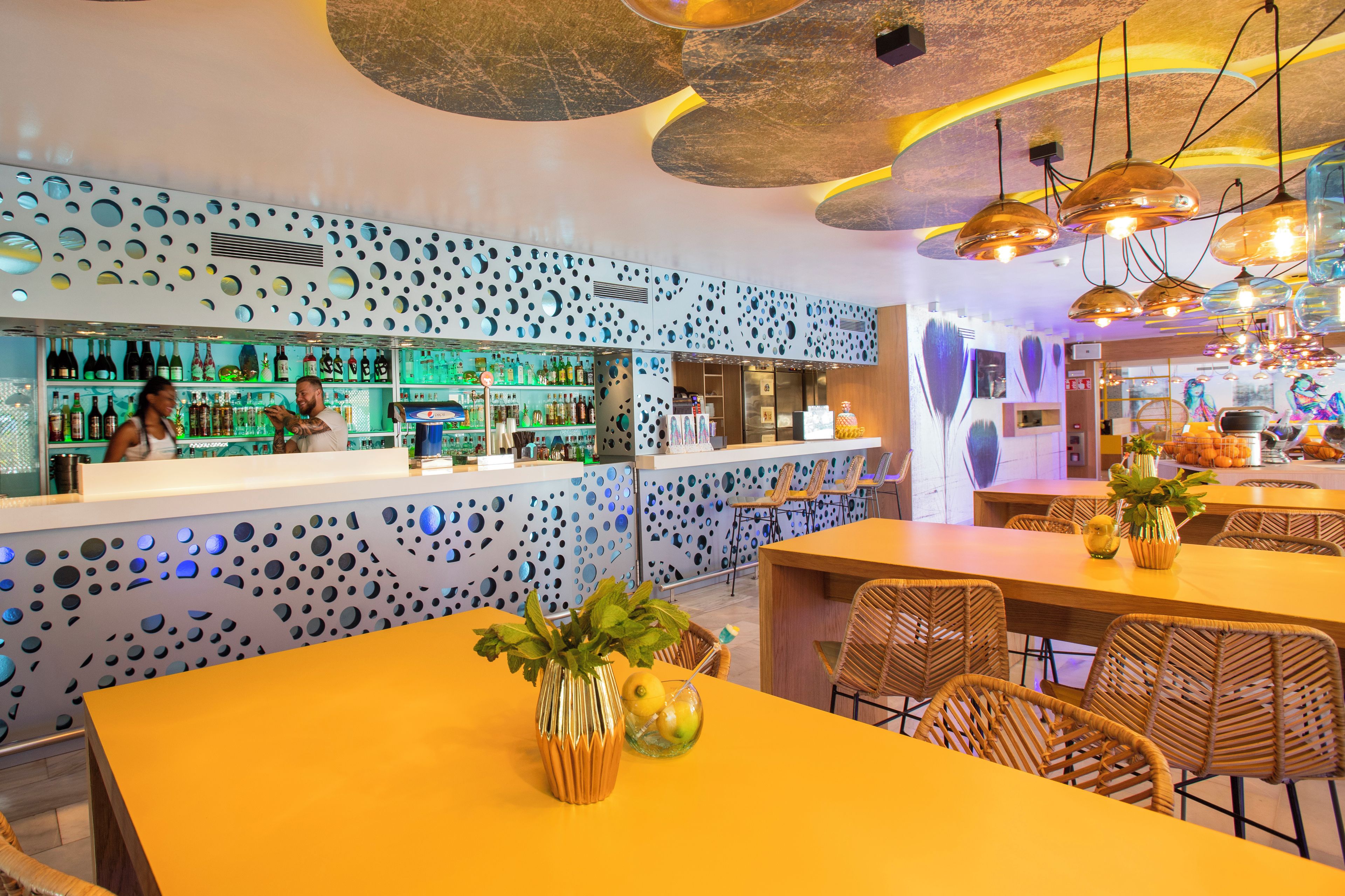 A bar area with a modern design, featuring a patterned wall and a variety of bottles on shelves.