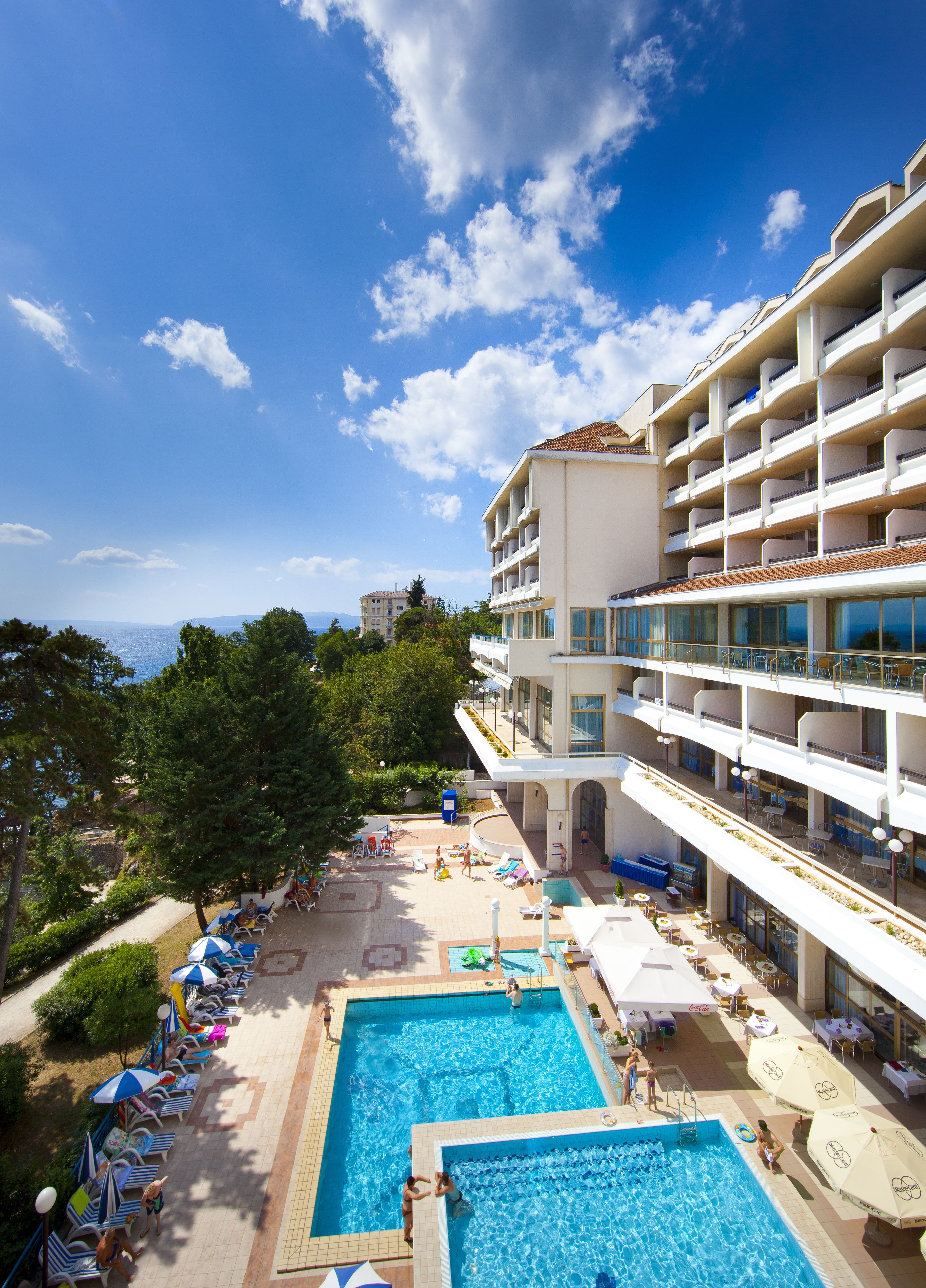 A hotel with a rooftop pool area, multiple swimming pools, and a view of the sea.