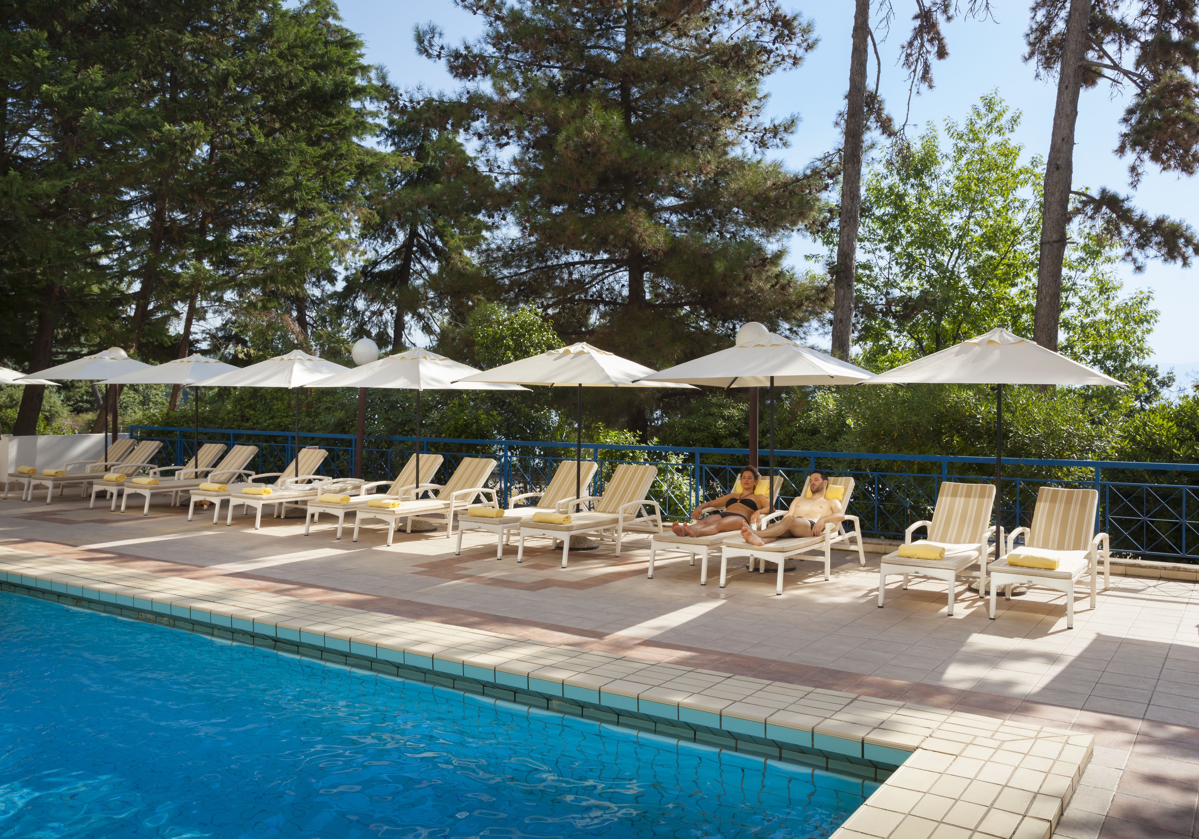 A poolside area with lounge chairs and umbrellas, surrounded by trees.