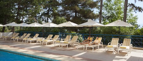 A poolside area with lounge chairs and umbrellas, surrounded by trees.