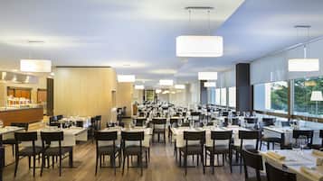 A spacious restaurant with multiple dining tables and chairs, large windows, and modern pendant lighting.