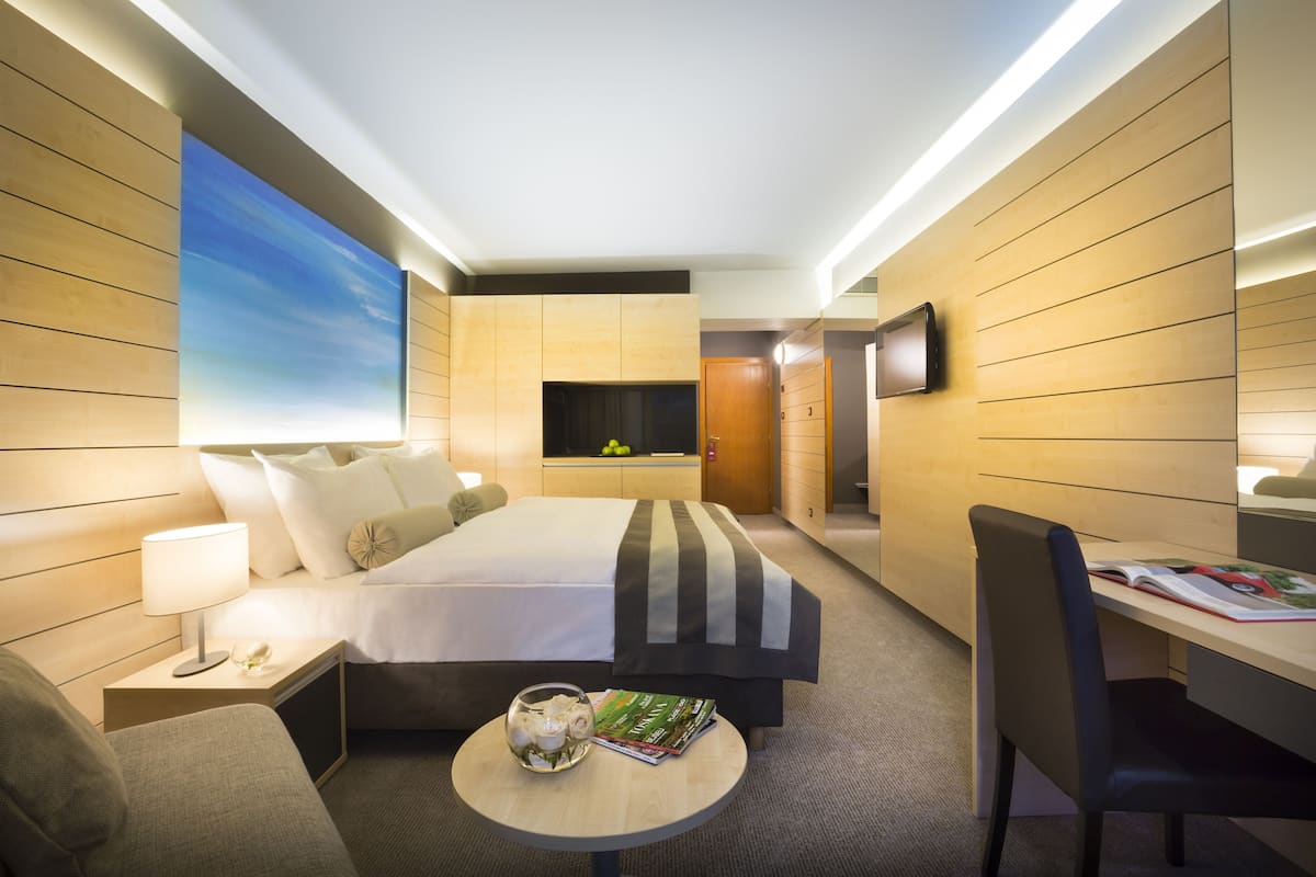 A hotel room with a bed, bedside table, lamp, chair, desk, and a TV.