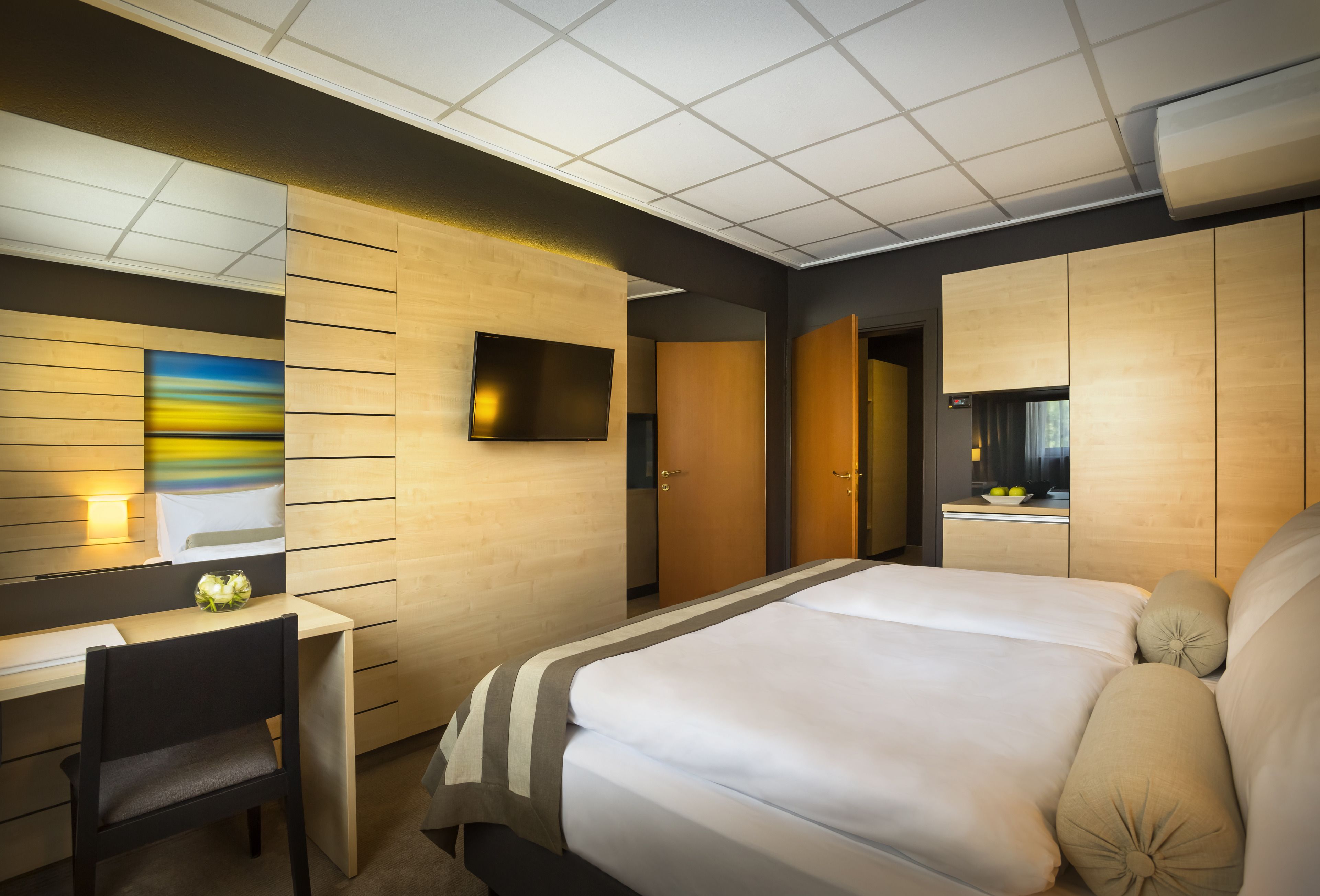 Una habitación de hotel moderna con una cama grande, un escritorio y un televisor de pantalla plana montado en la pared.