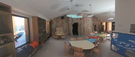 A spacious room with a large table and chairs, a bookshelf, and a wall with a rock-like texture.