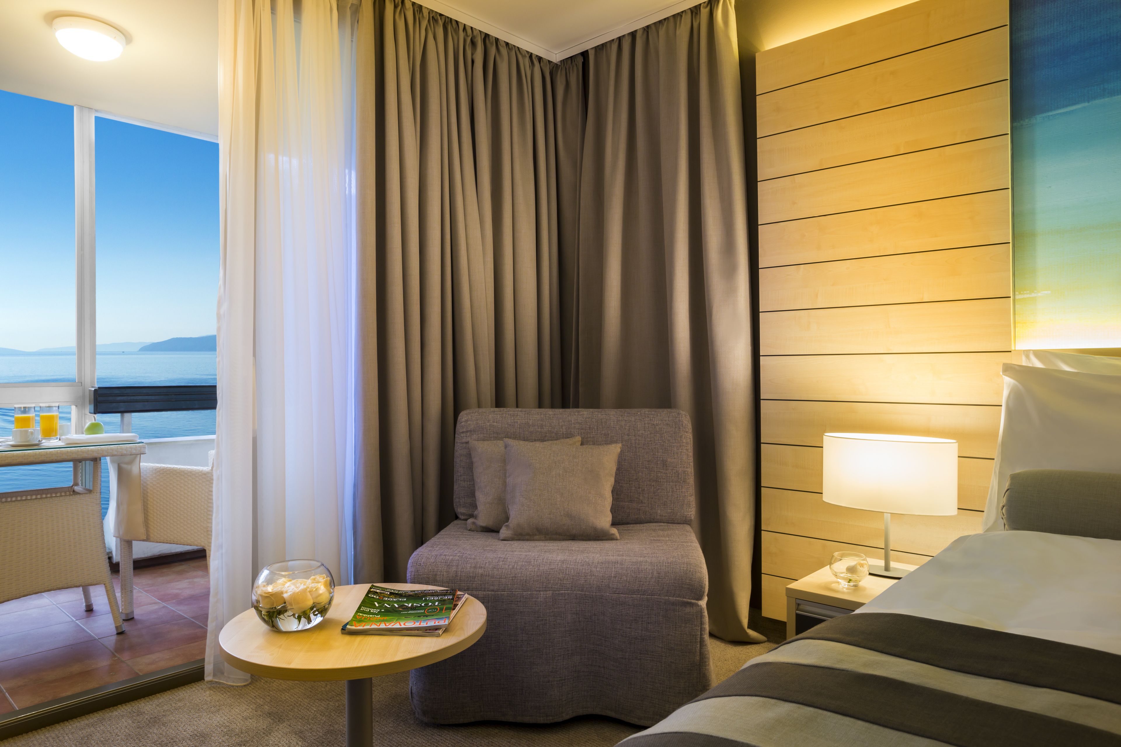 Une chambre d’hôtel avec un lit, un canapé, une petite table avec un livre et un verre, et une table de chevet avec une lampe.