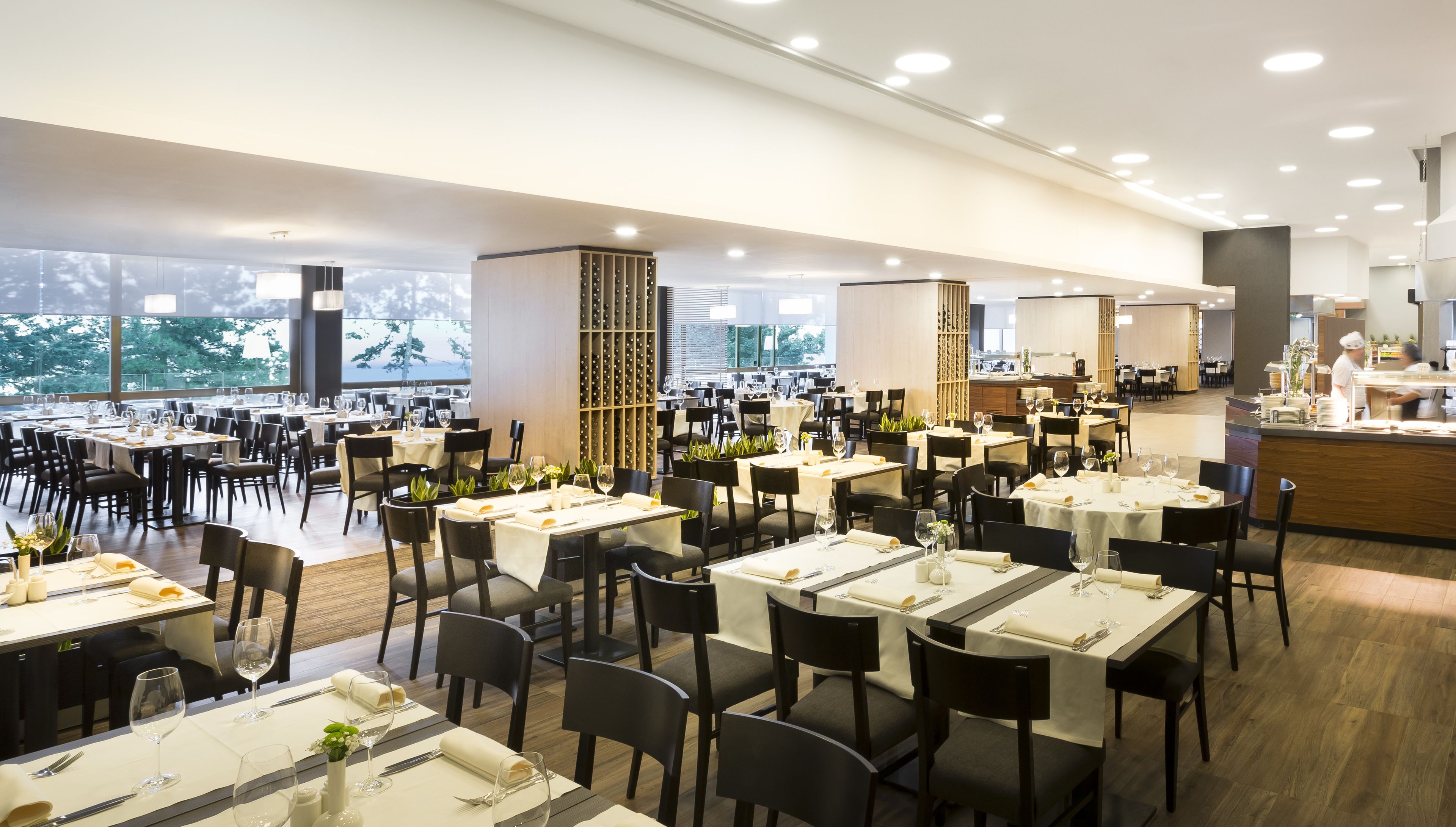 Un comedor amplio con varias mesas dispuestas para recibir a los huéspedes, grandes ventanales que ofrecen vistas y una decoración de estilo moderno.