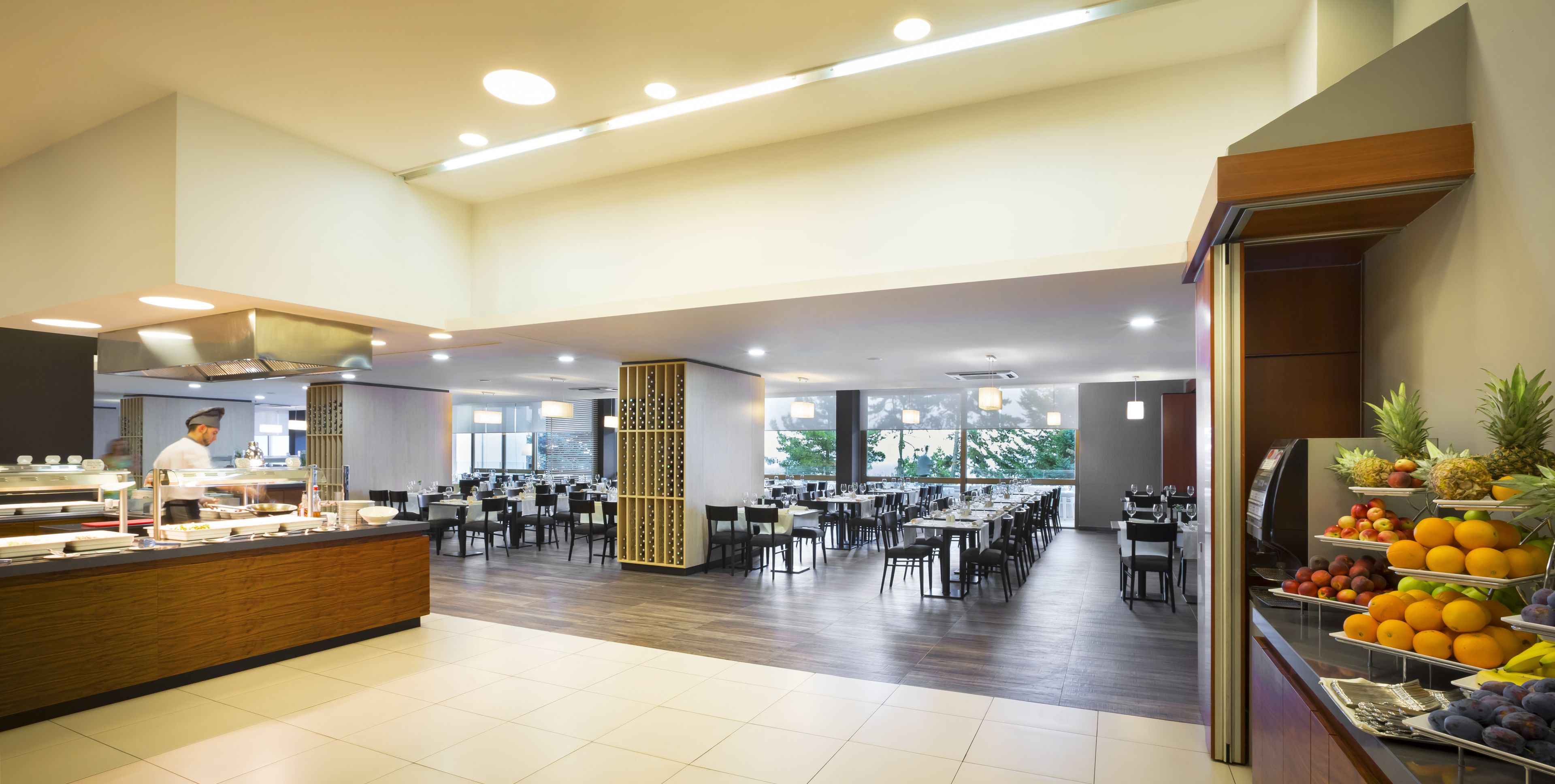 A spacious dining area with multiple tables and chairs, a buffet counter, and a fruit display.