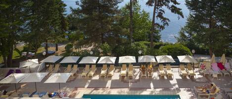 Ein Poolbereich mit zwei Schwimmbecken, Liegestühlen, Sonnenschirmen und Blick aufs Meer.