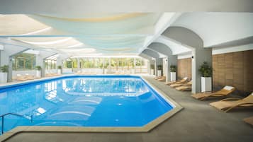 Una piscina interior con agua cristalina, rodeada de sillones de descanso y plantas en macetas.