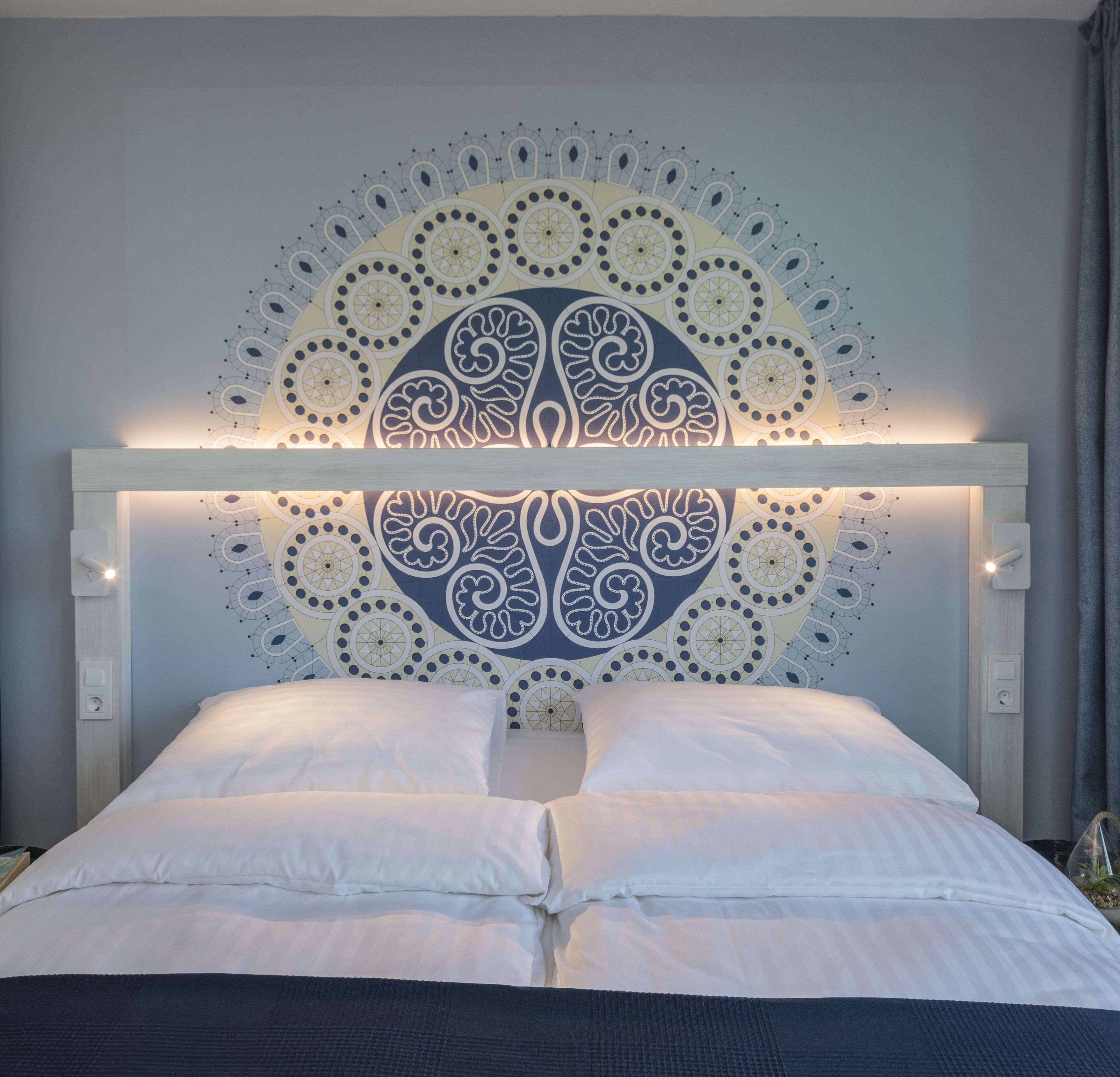 A bed with a white headboard and a decorative wall pattern.