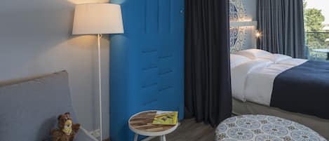 Habitación de hotel con una cama, un sofá, una mesita con una revista, una lámpara y un armario azul.