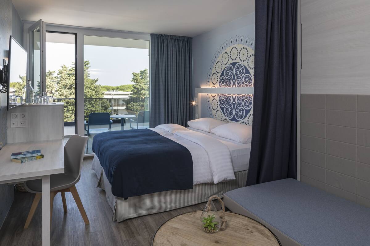 A modern hotel room with a bed, a desk, and a view of the outdoors.