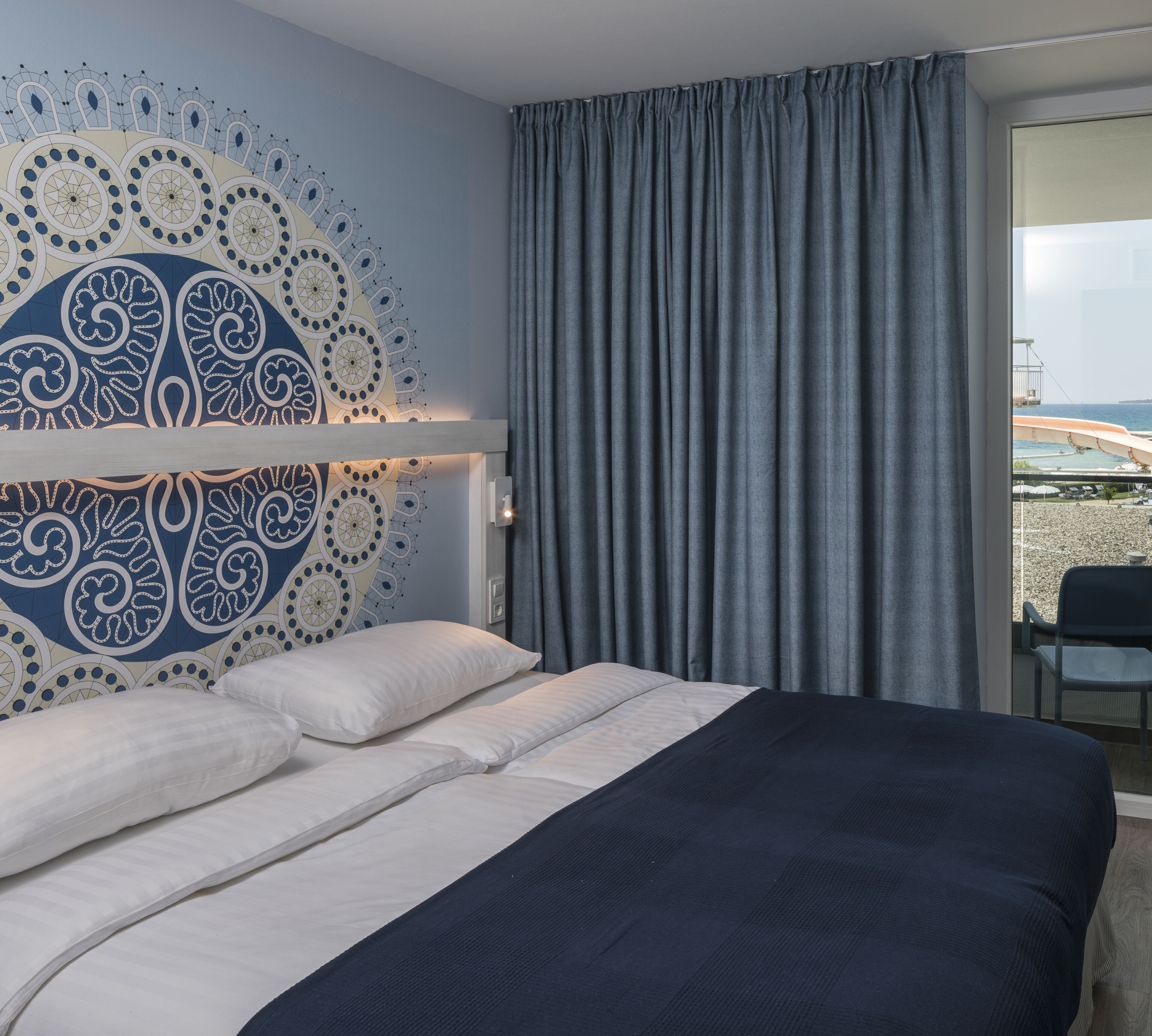 Una habitación de hotel con una cama, vistas al mar y un detalle decorativo en la pared.